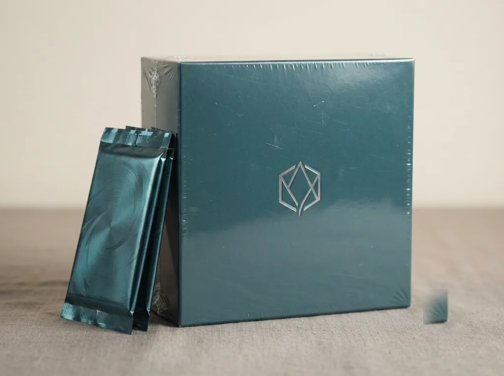 A sealed teal booster display box with three foil packs leaning against it