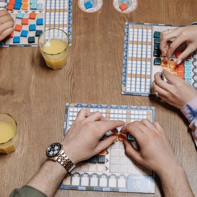 An overhead view of hands playing a tile game with drinks on the table